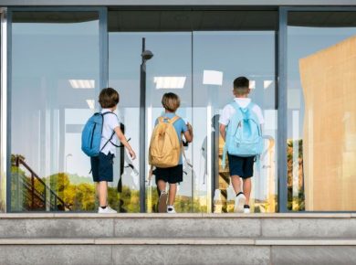três meninos de costas, em período de volta às aulas, entrando na escola