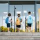 três meninos de costas, em período de volta às aulas, entrando na escola