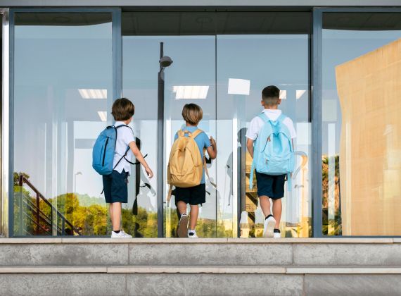 três meninos de costas, em período de volta às aulas, entrando na escola