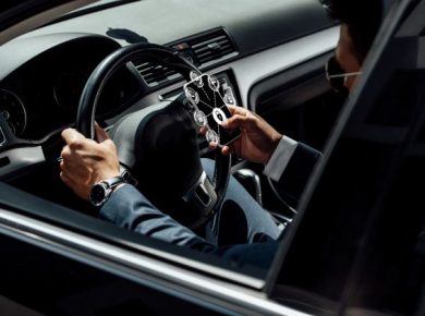 homem com terno em um veículo preto, com uma mão no volante e outra com o celular